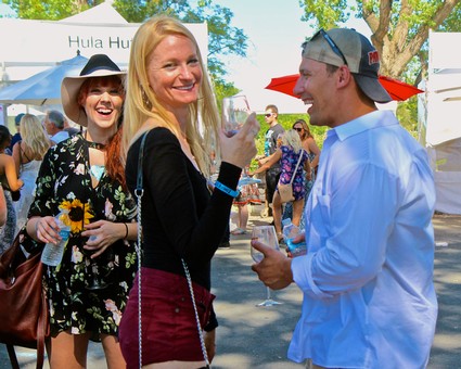 People enjoying wine at Lodi Winegrape Commission outdoor event with trees and tents in background.