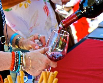 People pouring red wine into a glass at a wine tasting event in Lodi, California.