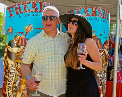 Couple enjoying wine at Lodi Winegrape Commission event with colorful circus-themed backdrop.