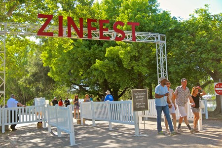 Visitors entering Zinfest wine festival at Lodi Winegrape Commission with trees and signage.