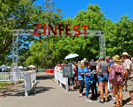 Crowd attending Zinfest event at Lodi Winegrape Festival with trees and blue sky in background.