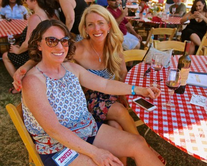 Two smiling women enjoying outdoor event at Lodi Winegrape Commission with wine and food.