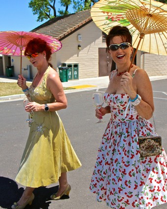 Two women enjoying the Lodi Winegrape Festival with parasols and wine glasses, celebrating local wine culture.