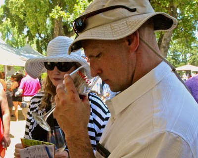 Man tasting wine at Lodi Winegrape Commission outdoor event with woman in background.