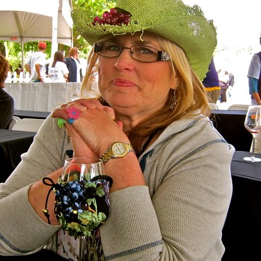 Woman enjoying wine at a Lodi Winegrape Commission event, wearing a green hat and glasses.