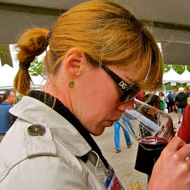 Woman tasting red wine at Lodi Winegrape Commission event, outdoor setting with attendees and tents in background.