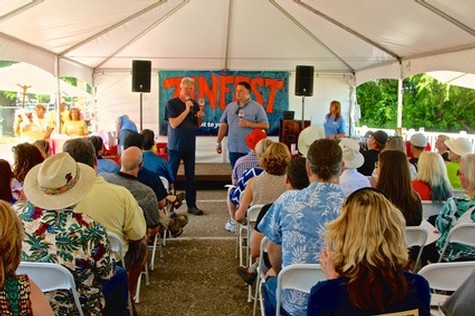 People attending a Lodi Winegrape Commission event under a tent with a speaker on stage and audience members seated.