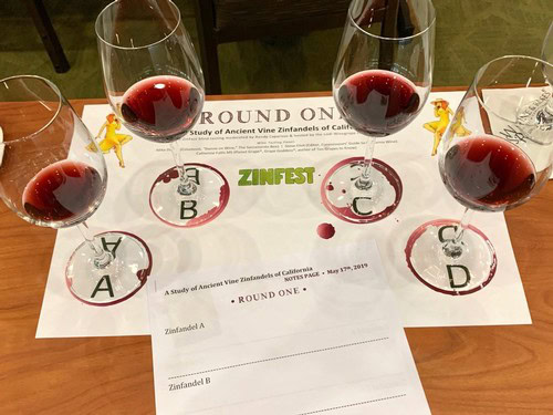 Four glasses of red wine on a table with a wine tasting sheet and yellow figurines.