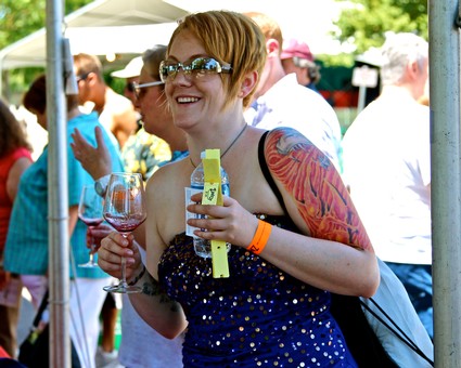 Smiling woman with tattoos enjoying wine at Lodi Winegrape Festival outdoors.