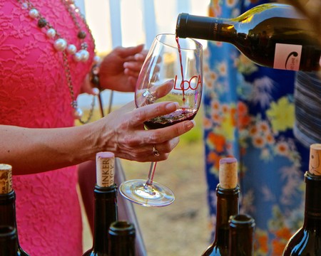Person pouring red wine into a glass at a Lodi wine event, with wine bottles on table.