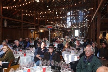 Attendees at a Lodi Winegrape Commission event enjoying a wine tasting in a rustic barn setting.