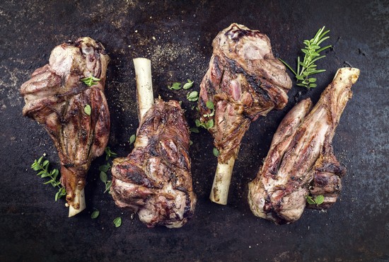 Four grilled lamb chops with herbs on a black surface, showcasing premium quality meat for wine pairing.