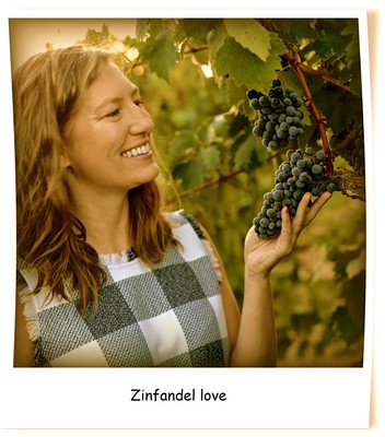 Woman enjoying grape harvest in Lodi wine vineyard, smiling and holding a bunch of ripe Zinfandel grapes.