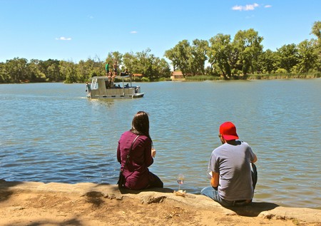 Two people sitting by the lake watching a boat on the water in Lodi, California.