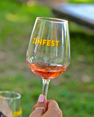 Glass of rosé wine with ZINFEST logo, outdoor setting, promotional event for Lodi wine region.