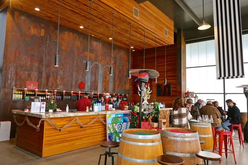 Modern wine tasting room with wooden accents, wine barrels, and patrons enjoying wine at Lodi Winegrape Commission.
